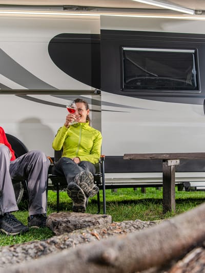 a couple boondocking without hookups in their rv in the woods near a campfire drinking wine